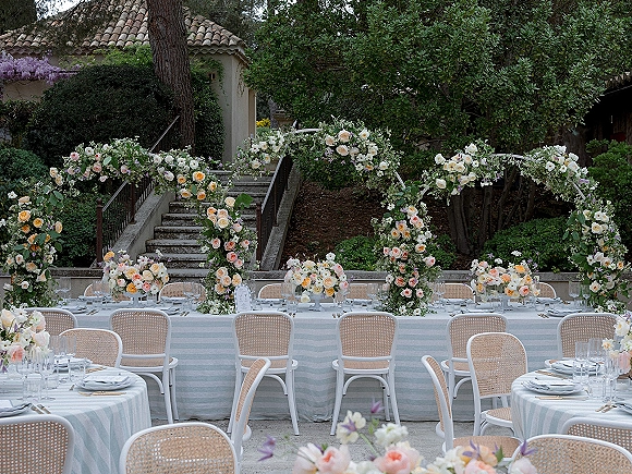 Reception tablescape with a garden reception tablescape, striped linens, rose garlands and a floral arch in a courtyard by stone steps