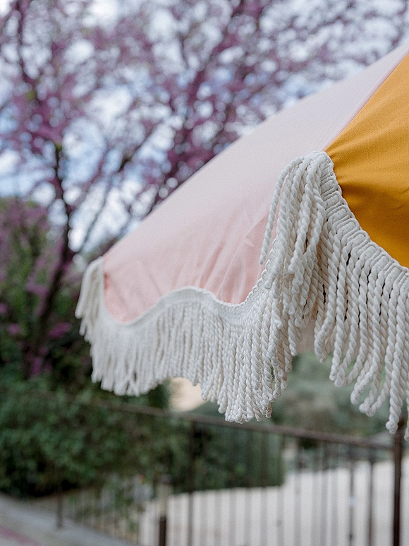 Tent draping detail with wedding tent draping and fringe trim, soft fabric canopy against flowering trees, greenery, and a fence outdoors