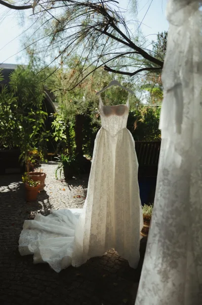 Wedding dress, lace wedding dress hanging on a hanger with a long train in a sunlit garden courtyard with potted plants and trees