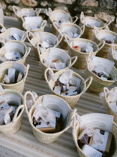 Wedding welcome baskets arranged as guest welcome gifts with welcome cards on a striped tablecloth against a stone wall.