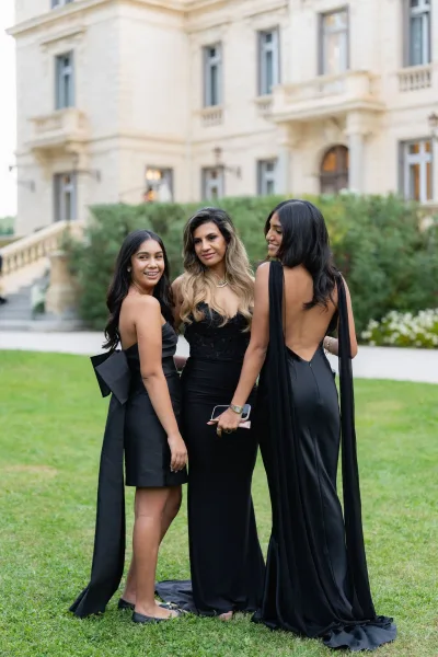 Wedding guest portrait of friends at wedding on a garden lawn before a mansion facade, wearing gowns with a bow detail.