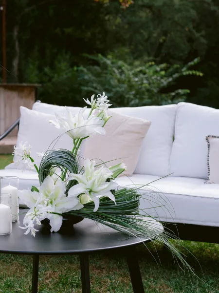 Wedding lounge decor styled for an outdoor reception lounge, highlighted by an arrangement of white lilies on a lawn amid garden trees and shrubs.
