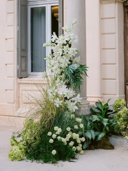 Wedding floral installation climbing a stone column, a floral column installation featuring white lilies arranged in an organic, asymmetrical cascade.