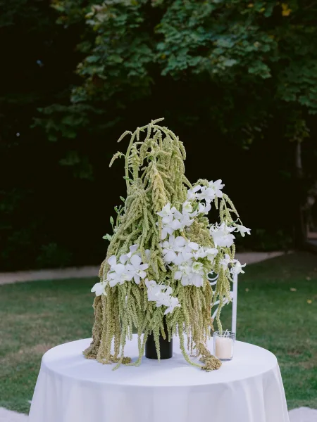 Wedding centerpiece, an orchid centerpiece set outdoors against garden trees, grass lawn, and a dark hedge.