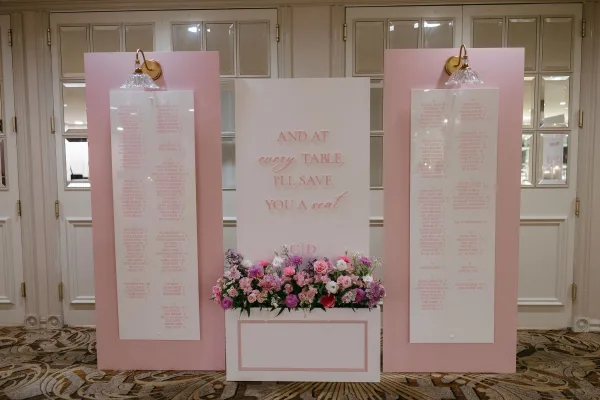 Wedding seating chart with pink display panels and acrylic guest list boards, styled with a floral arrangement in an indoor foyer with wall sconces