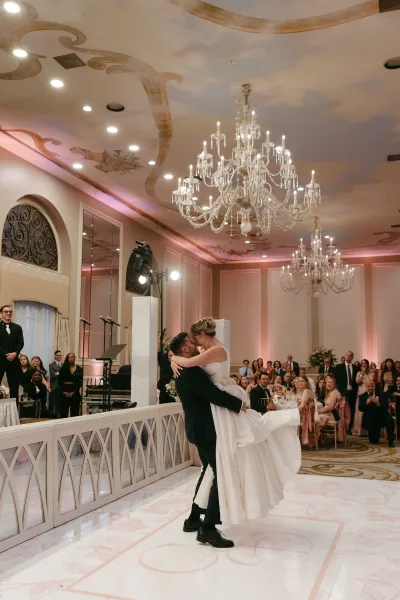 First dance moment as the groom dips and kisses the bride in a strapless ball gown on a ballroom floor beneath crystal chandeliers