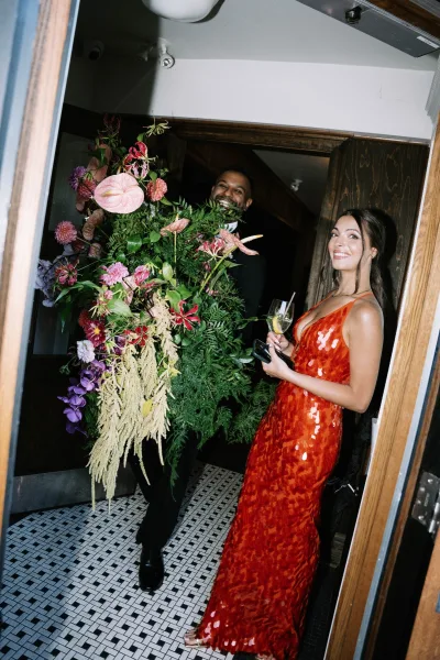 Reception candid during wedding cocktail hour as a smiling guest in a sequin gown pauses in an indoor hallway with patterned tile floor.