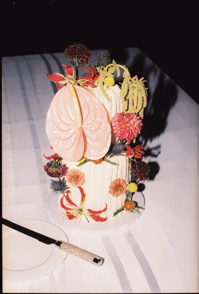 Floral wedding cake, a two-tier wedding cake with a sculptural anthurium accent cascading along the tiers against a dark, shadowed background.