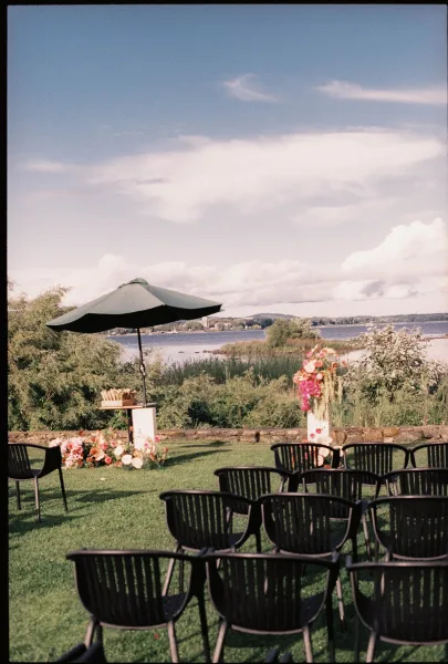 Outdoor ceremony setup showcasing lakeside ceremony decor with floral arrangements, set by a calm lake and stone wall under an open sky.