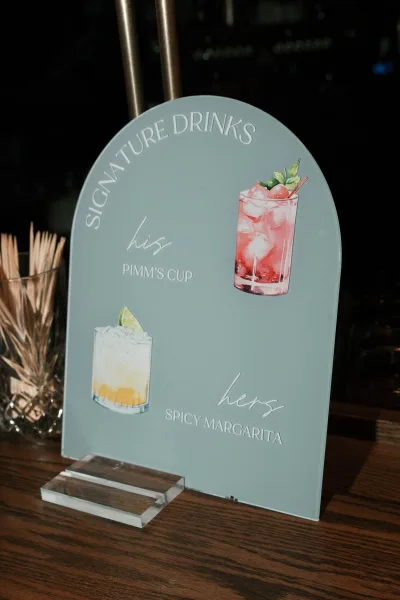 Signature drink sign presented as a wedding bar sign, an arch sign on a wood bar counter against a dark bar backdrop.