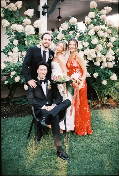 Wedding party portrait of bride and groom with friends, the bride cradling a bridal bouquet before hydrangea bushes and porch columns.