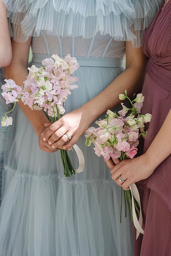 Bridesmaid bouquets of pink sweet peas tied with white ribbon wraps, held by bridesmaids in pleated chiffon and tulle dresses outdoors