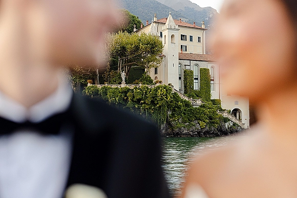 Wedding venue exterior with ivy-covered walls and stone staircase, overlooking a lake with mountains beyond under open sky