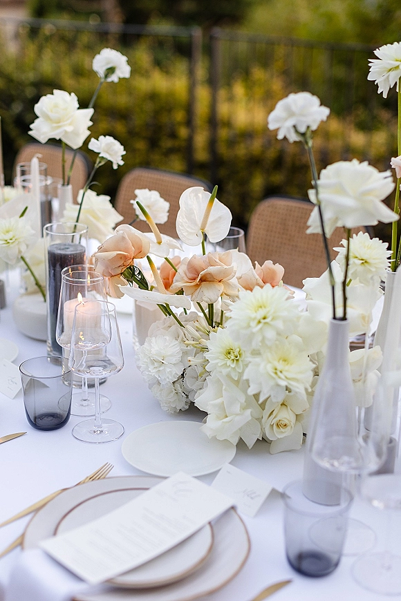Reception tablescape with wedding table decor featuring white floral centerpieces, blush roses, taper candles, gold flatware on linen outdoors