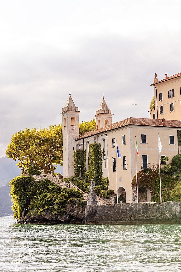 Wedding venue exterior of a historic wedding venue with ivy, stone staircase and arched doorway, overlooking a lake with mountains under cloudy sky