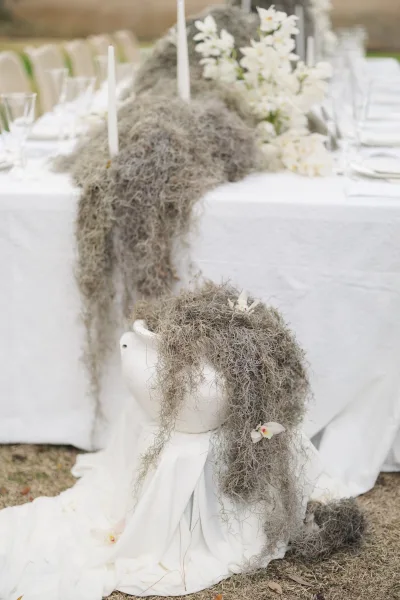 Reception tablescape with white wedding table decor, taper candles, Spanish moss runner, and white florals on an outdoor lawn with leaves