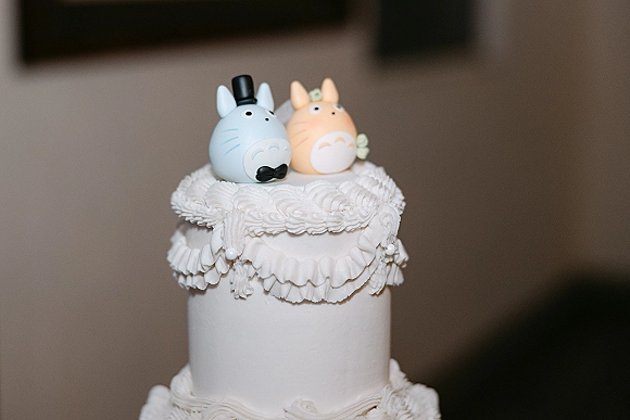 Wedding cake with cute wedding cake topper figurines in tuxedo and top hat, white rosette and ruffle icing, green leaf detail indoors