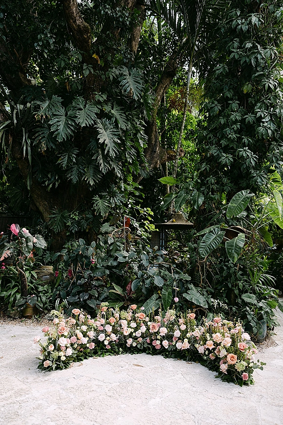 Ceremony floral arrangement with grounded ceremony flowers in blush and pink roses and greenery bordering a stone path in a tropical garden
