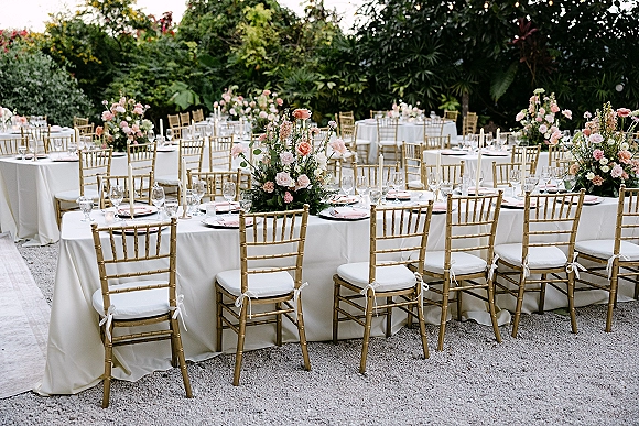 Reception tablescape for an outdoor wedding reception with white linens, gold chiavari chairs, blush rose greenery centerpieces and taper candles on a gravel patio