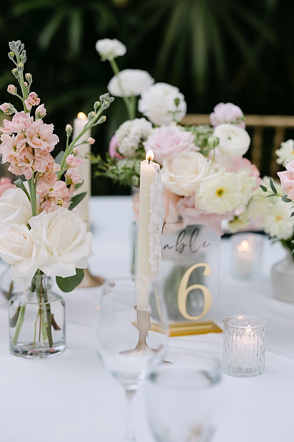 Reception tablescape with wedding table centerpiece of pink and white florals in glass vases, taper candles, and place cards outdoors