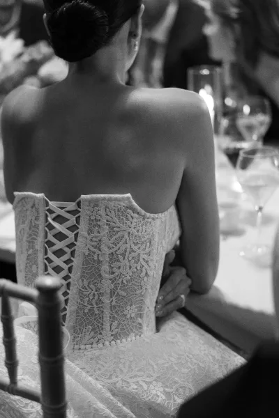 Wedding dress back with lace corset back wedding dress lacing as the bride hugs a guest at a reception table with candles and wine glass