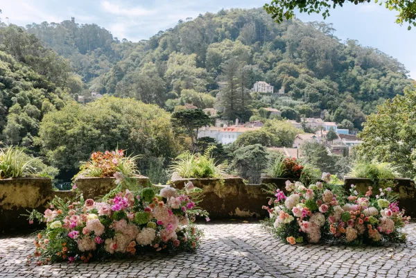 Ceremony floral decor with ground floral arrangements of hydrangeas, roses, and greenery lining a stone terrace, forest hillside beyond