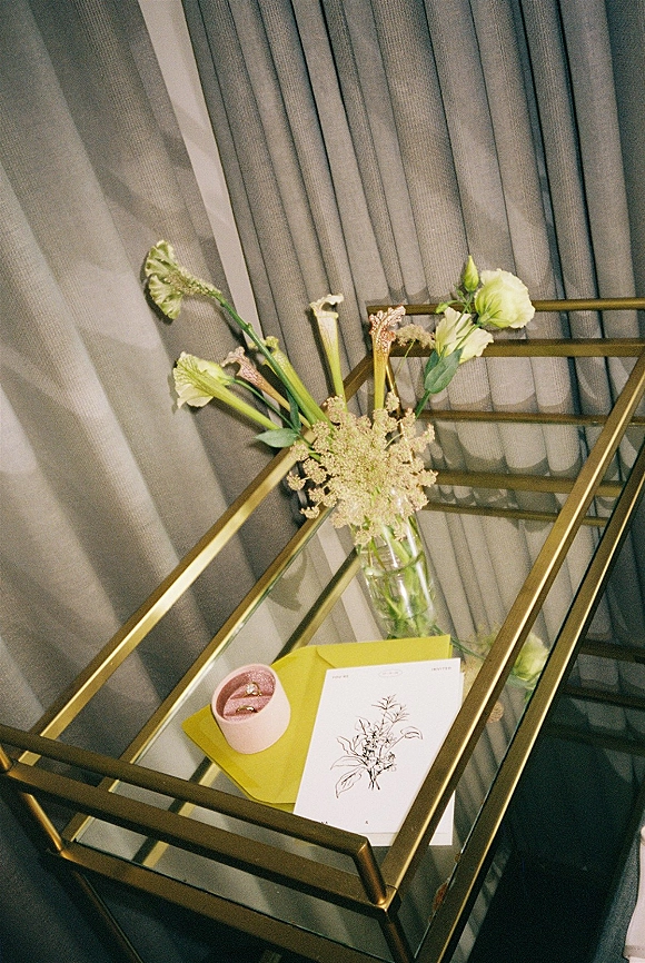 Wedding invitation suite with minimal wedding invitations, green envelope and pink wax seal beside vase flowers on a gold glass table