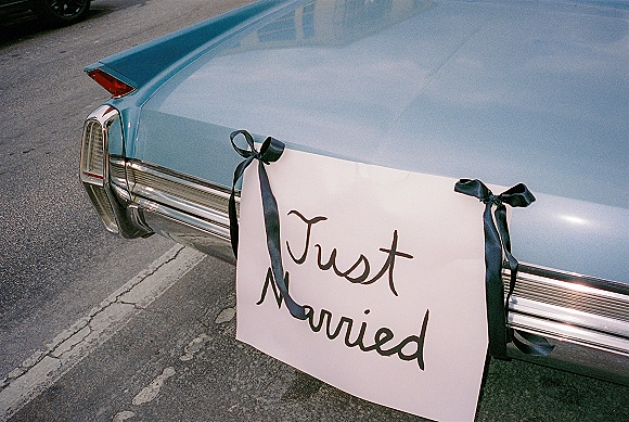 Wedding car sign reading just married on a white poster with black ribbon bows on a vintage car rear bumper by the curb