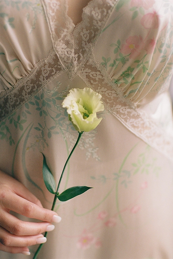 Bridal lingerie in soft indoor light, a lace bridal lingerie floral slip dress with a single flower stem and natural nude manicure