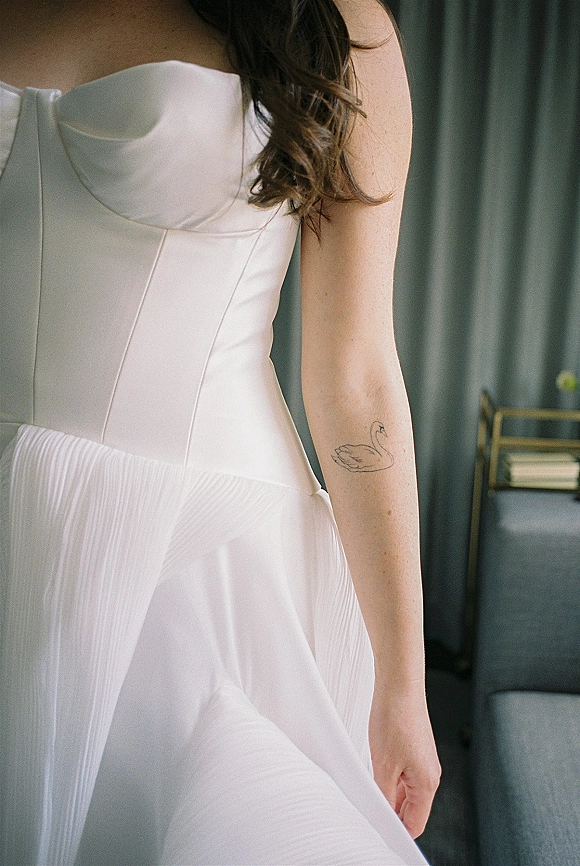 Wedding dress close-up of a corset wedding dress with boned bodice and pleated chiffon skirt, showing the bride’s arm tattoo indoors