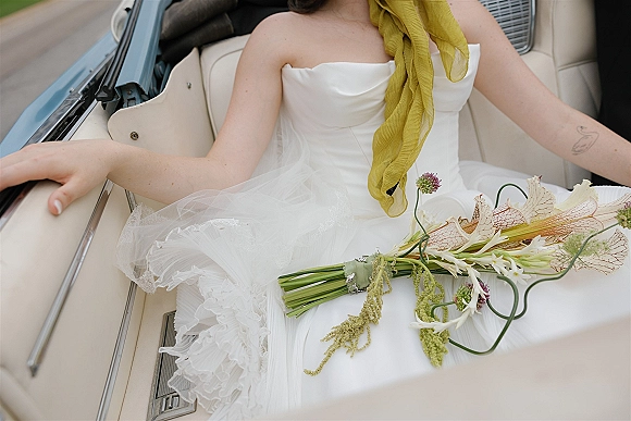 Bridal portrait of bride in convertible holding a calla lily bouquet on her lap, wearing a strapless tulle dress on a road