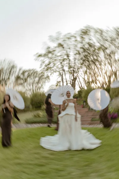 Bridal portrait of a bride holding parasol in a strapless wedding dress with choker and bracelets on garden steps at sunset