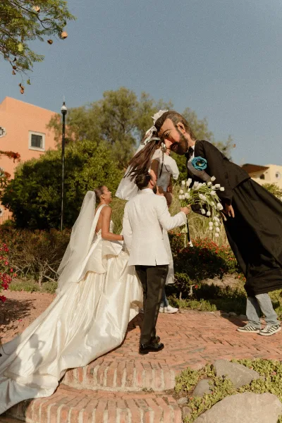 Wedding couple portrait of bride and groom walking on brick steps, bride in long veil holding dress train beside oversized puppets in garden setting