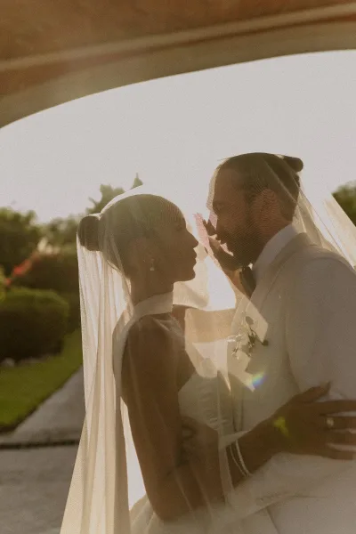 Wedding couple portrait of bride and groom silhouette as she touches his face under her veil, backlit at sunset on a garden walkway
