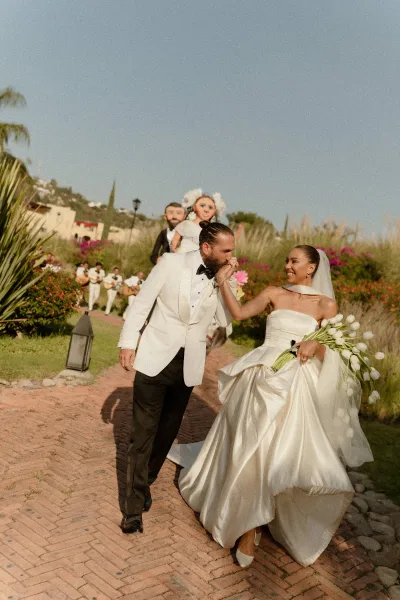 Wedding couple portrait of bride and groom walking on a brick walkway, groom kissing her hand as she holds a tulip bouquet in a garden setting