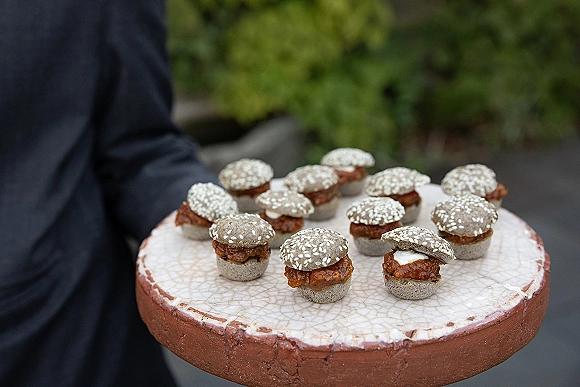 Wedding appetizers on a ceramic platter, mini slider buns with sesame seeds served as passed hors d'oeuvres at an outdoor cocktail hour