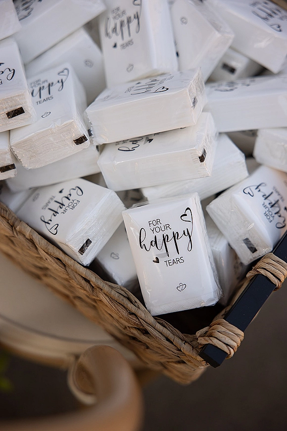 Happy tears packets with wedding happy tears tissues in a wicker basket, printed black-and-white labels displayed on a tabletop