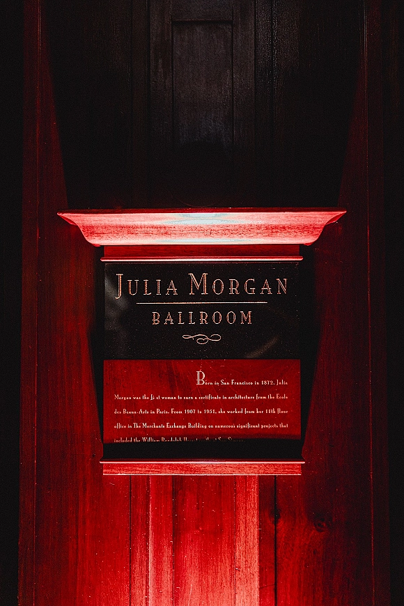 Wedding venue sign with engraved lettering on a wall plaque in a sign frame, mounted on dark wood paneling with moody red lighting