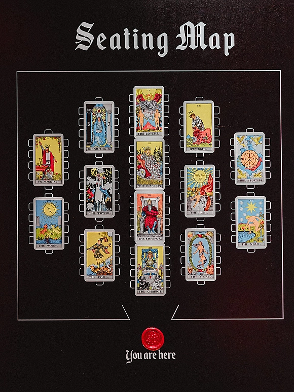 Wedding seating chart with tarot seating chart illustrations, gothic lettering, and a red wax seal on a printed sign against a black backdrop