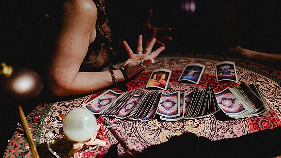 Tarot card reading at a wedding tarot reader table, hands with bracelets and rings arranging cards beside a crystal ball in dim light