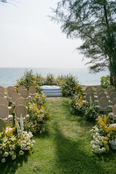 Outdoor ceremony setup with coastal ceremony decor, centered on a round platform on a grass lawn with the ocean and open sky beyond.