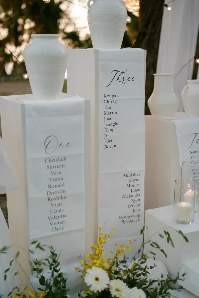 Seating chart display serving as the wedding seating chart, accented with yellow flowers beneath trees and warm string lights.