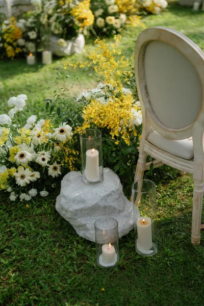 Ceremony aisle decor featuring garden ceremony flowers in low arrangements beside glass vases, set on a grass lawn amid lush garden plants.