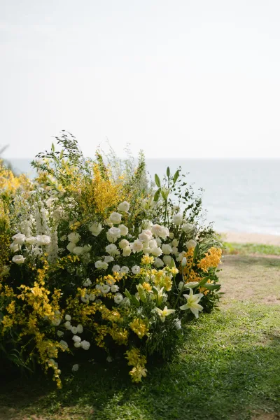 Ceremony flowers arranged as a ground floral installation of roses line the grass lawn with the ocean and open sky as a serene backdrop.