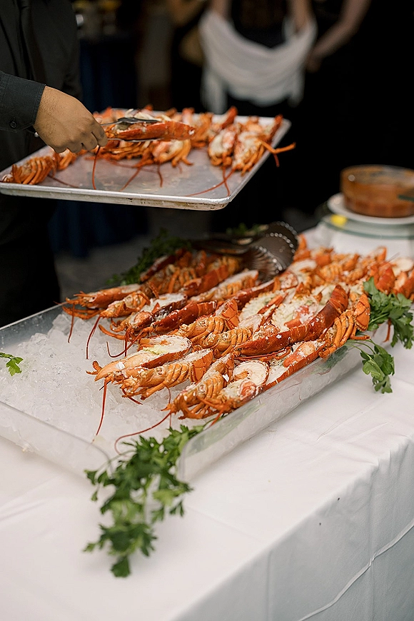 Wedding seafood display featuring lobster on crushed ice with parsley garnish and serving tongs on a white tablecloth at indoor reception