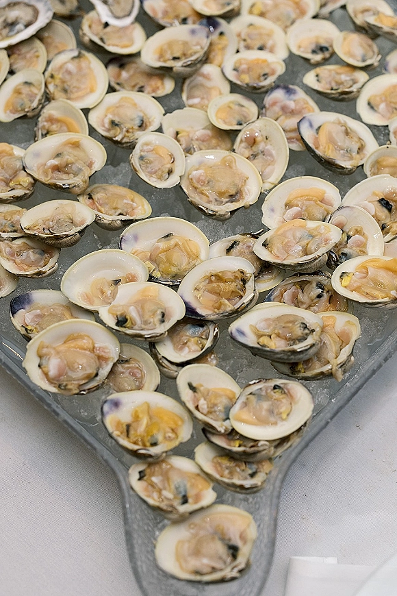Wedding raw bar with raw bar clams on ice in a serving tray, clams on the half shell arranged over a white tablecloth