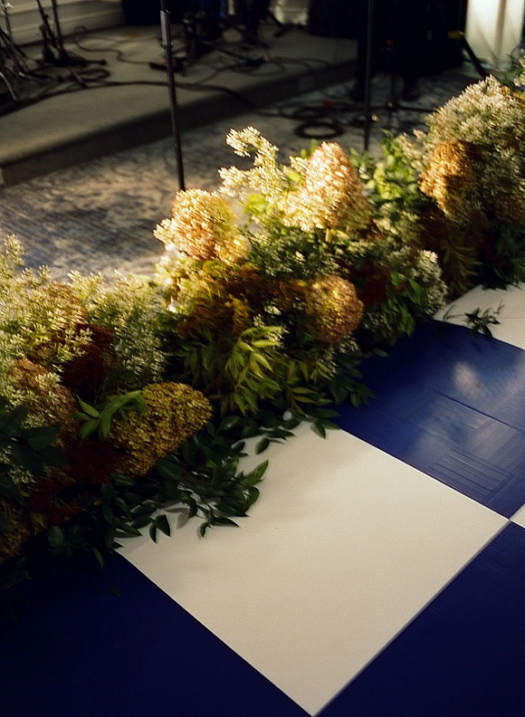 Wedding floral arrangement with greenery wedding garland and dried florals set along carpeted stage steps near microphone stands and cables