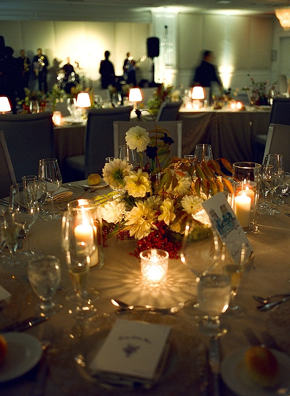 Reception tablescape with a wedding table centerpiece of low florals, pillar and votive candles, and place settings in a softly lit banquet hall