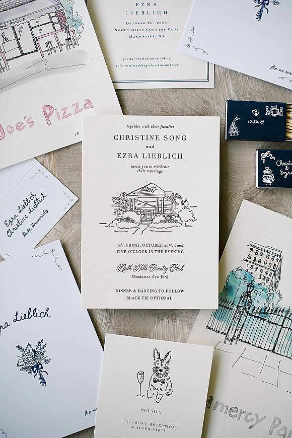Wedding invitation suite flat lay with blue ink calligraphy, venue sketch, RSVP cards, and envelope on a linen fabric backdrop