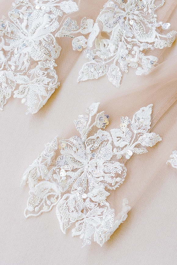 Wedding dress lace with lace appliqué, floral embroidery, and beading over nude mesh fabric, with subtle sequins catching the light